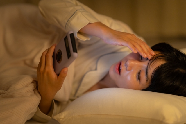 寝る前にスマホをいじる女性