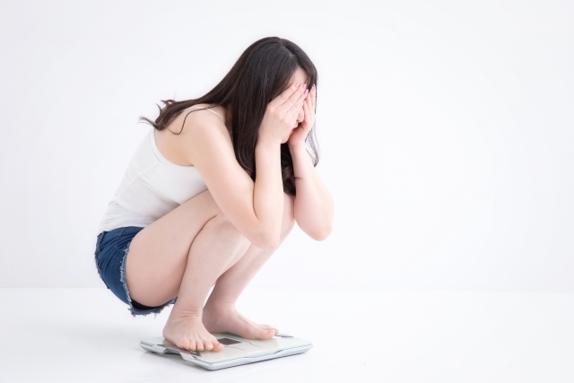 体重計に乗りダイエットに悩む女性